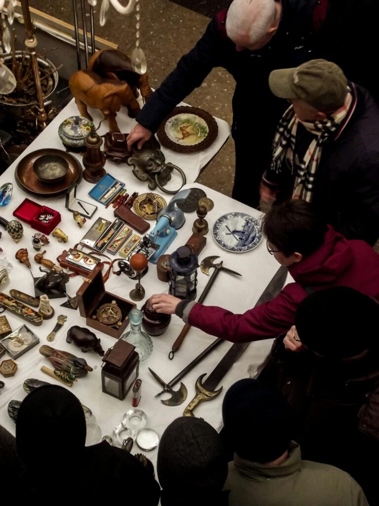 Group of people inspecting vintage antiques and collectibles at a bustling flea market.